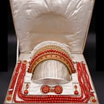 Gioielli 25 Telearte gioielli d'arte - Grande parure napoleonica in corallo mediterraneo, oro e perle Importante parure in oro giallo 9 kt composta da collana a tre fili, due bracciali, una coppia di orecchini, una fibbia e un pettine intercambiabile, uno in corallo e uno in perle. Le sfere sfaccettate sono interamente realizzate in corallo rosso del Mediterraneo, le fermezze in oro giallo. Rilevabile l’assenza di una perla dal pettine; con custodia originale